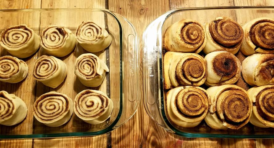A photo of two pans of cinnamon rolls - the left side hasn't been baked yet and the right side has just come out of the oven.